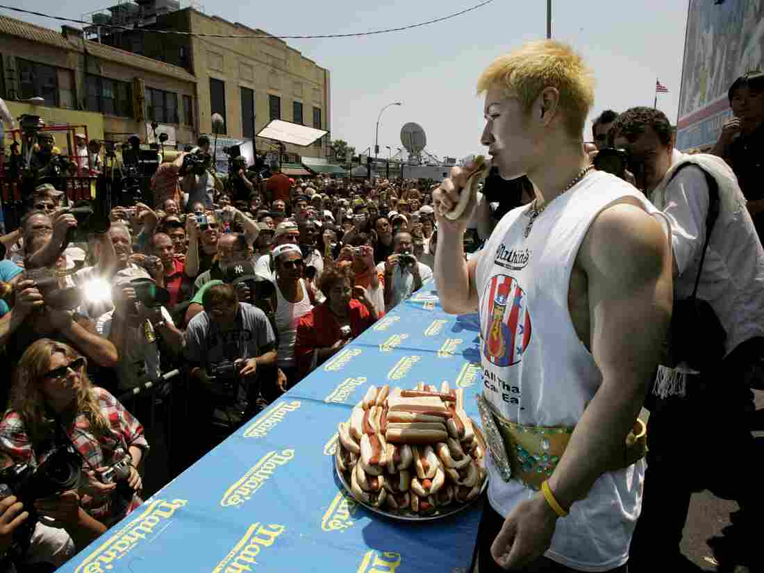 Kobayashi holds a hot dog as photographers in a large crowd snap pictures.