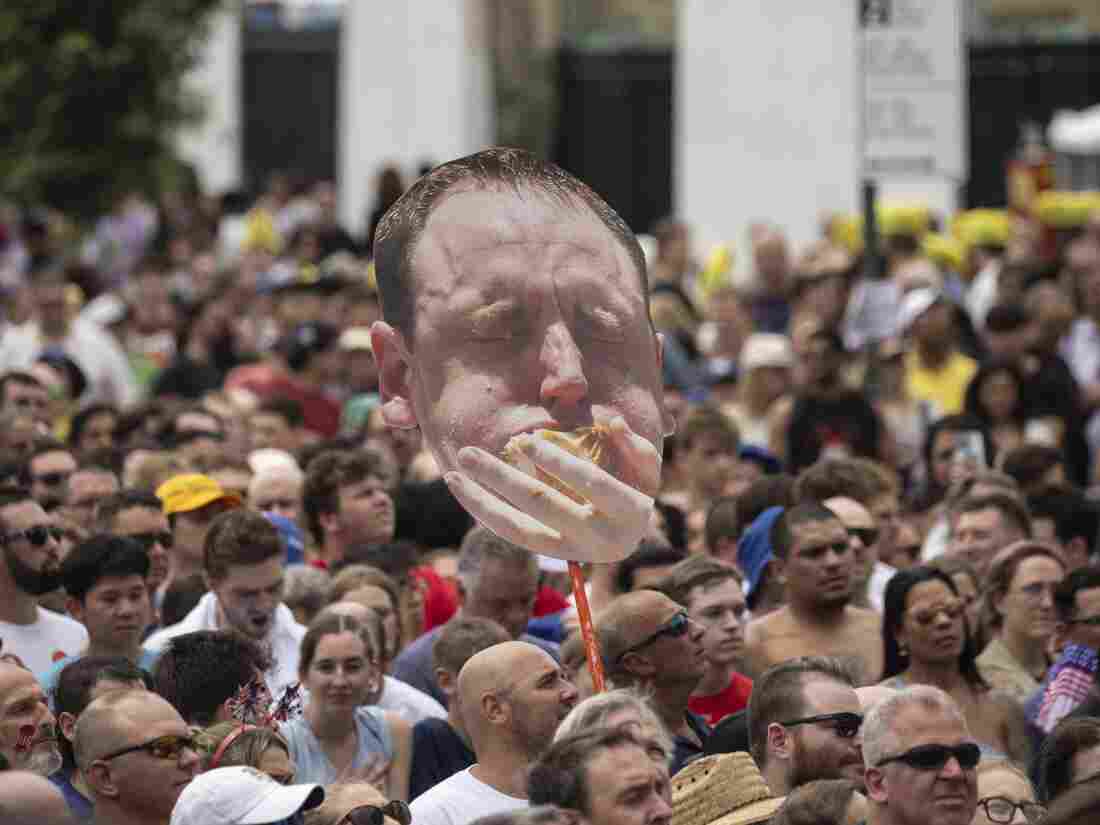 A spectator in the crowd holds up a huge cardboard cutout of Joey Chestnut's face. 